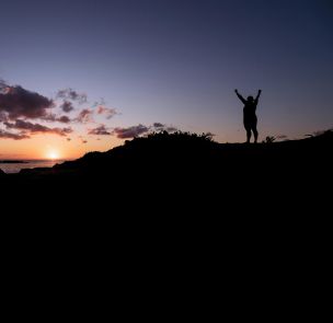 Silhouette of a person celebrating at a stunning sunset by the ocean.